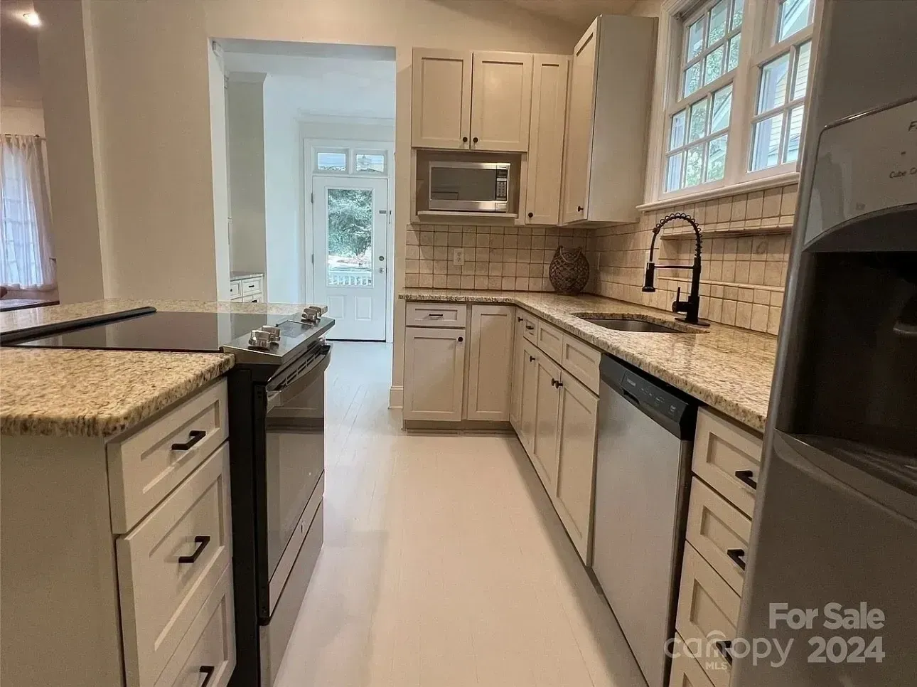 Bright galley kitchen with white cabinets, granite counters, stainless appliances, and tile backsplash