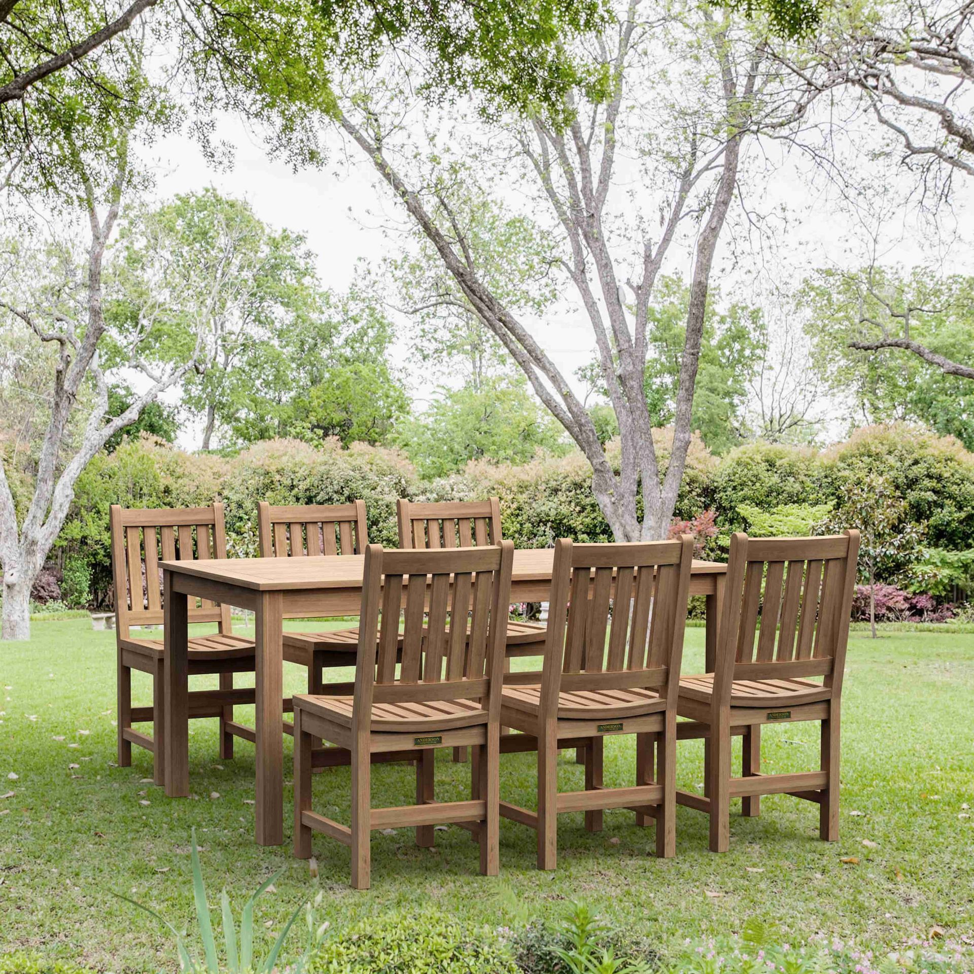 Wooden outdoor dining table and chairs on a grassy lawn beneath trees