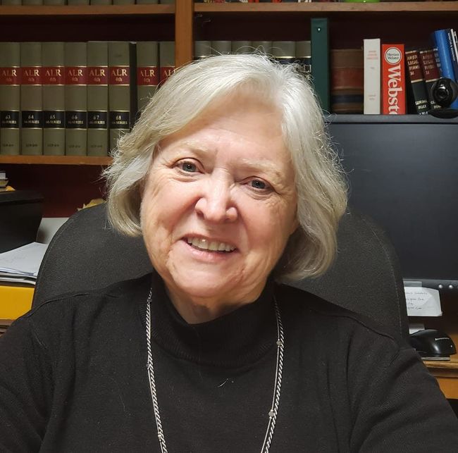A woman in a black turtleneck sits in front of a webster bookshelf