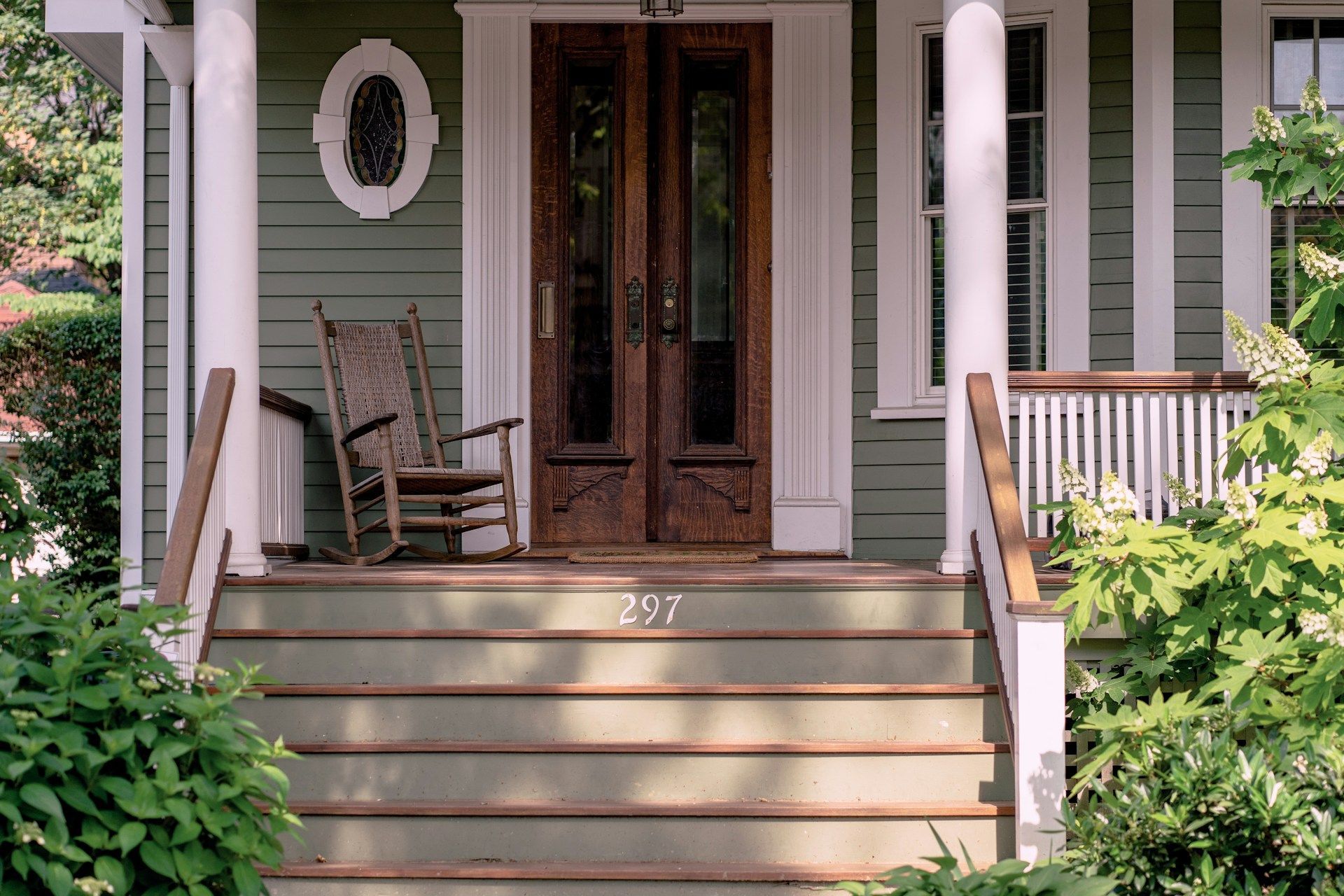 A green house with a rocking chair on the porch