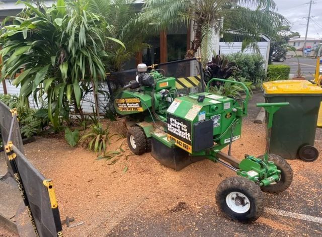 a Green Stump Grinder is Sitting in a Parking Lot Next to a Trash Can — Chris Hackett Tree Services In Ballina, NSW