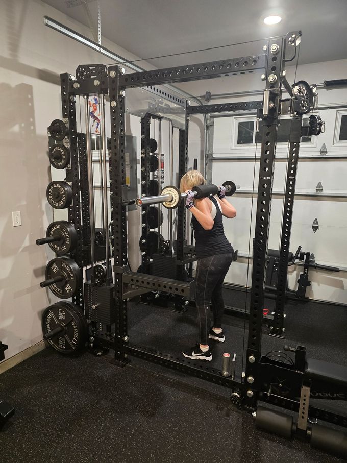 Woman squatting with barbell in a home gym, inside a weight rack.