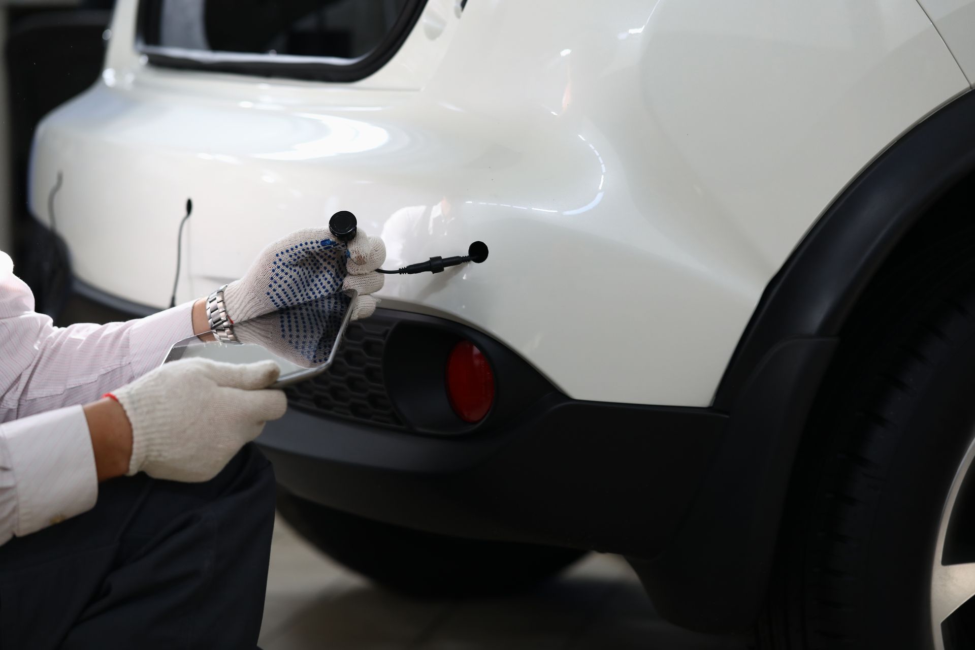 Person applying paint or touch-up to a white car’s rear bumper with a tool and protective cloth