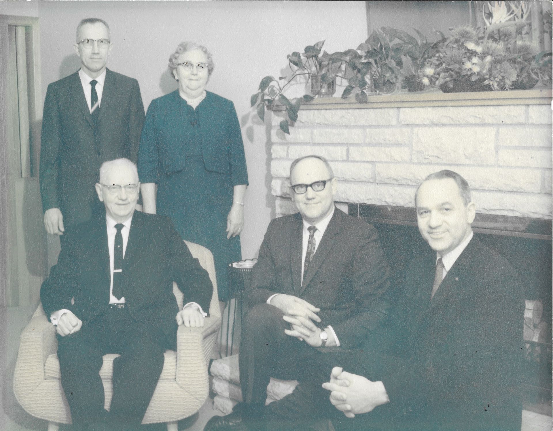 Five people pose in a living room beside a fireplace, with three seated and two standing behind them.