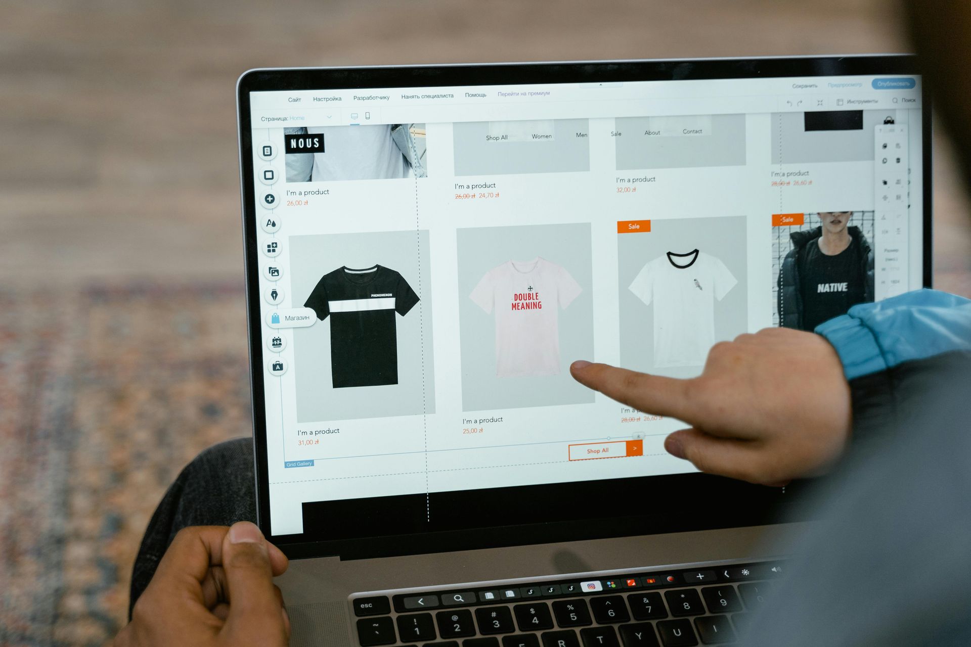 A close-up view of a person pointing at a t-shirt design option on a laptop screen featuring various clothing templates.