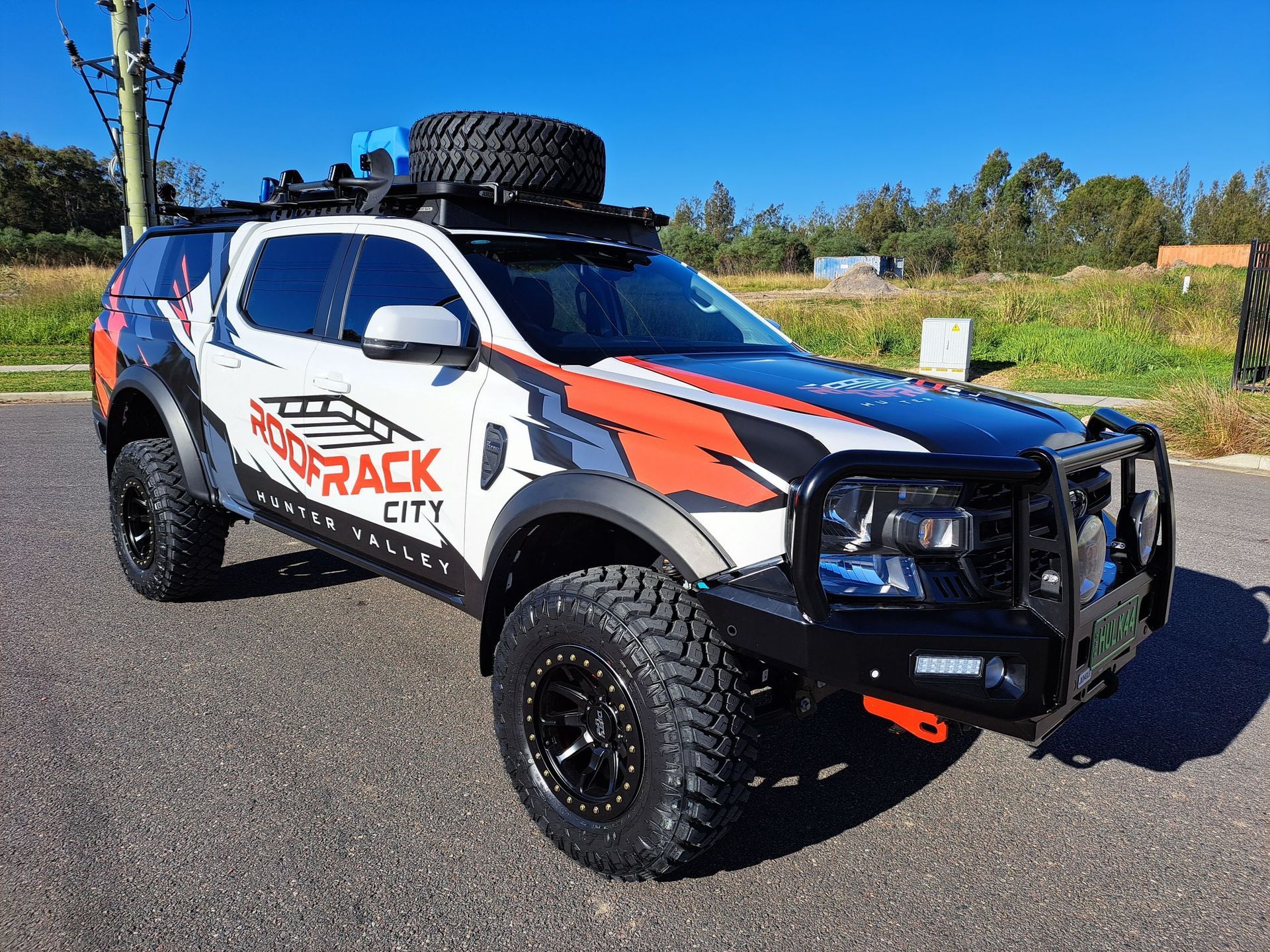 Off-road customized white, orange, and black SUV with roof rack, bumper, and large tires parked outdoors on pavement.