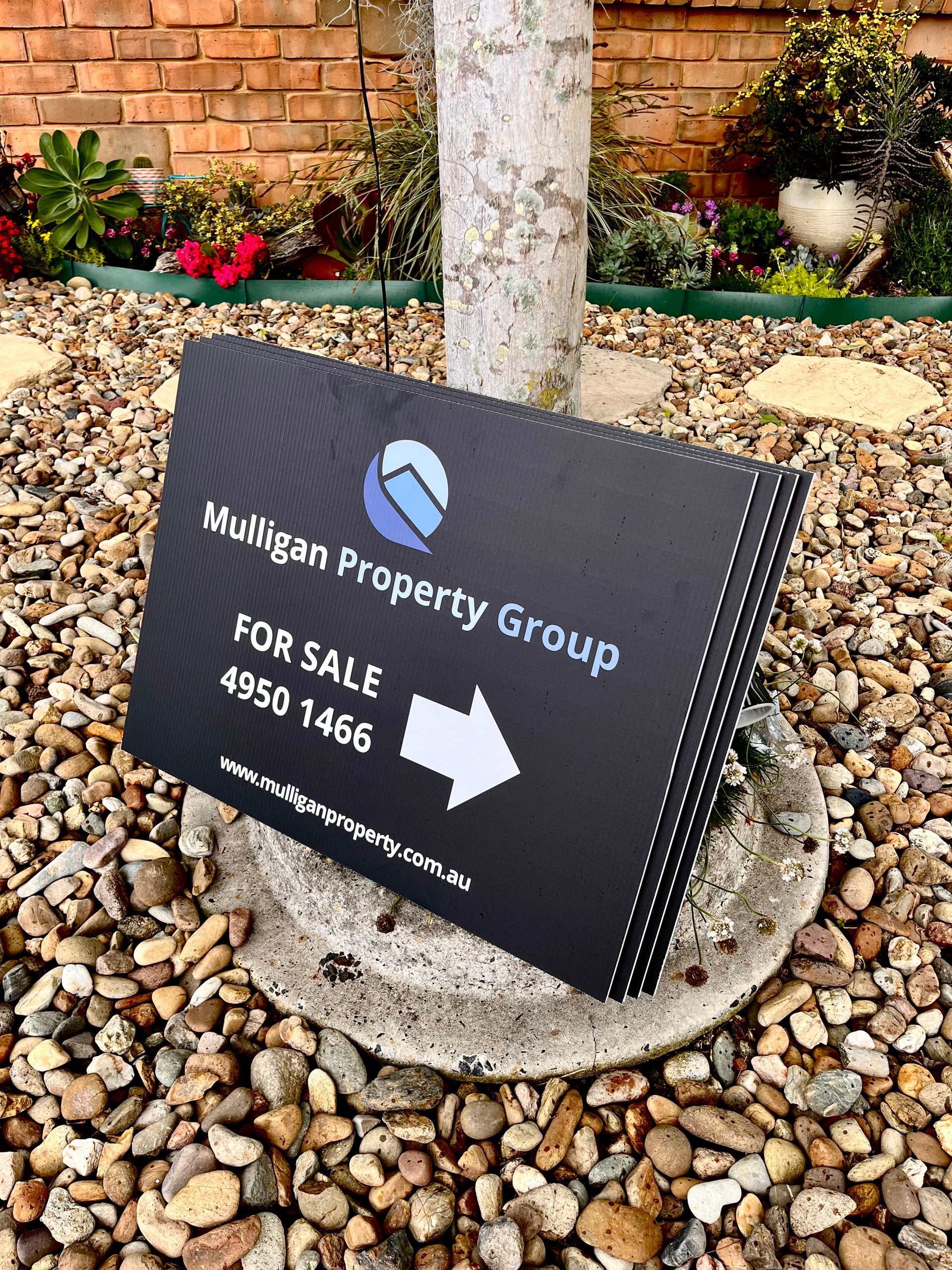 Real estate sign leaning against a tree, with