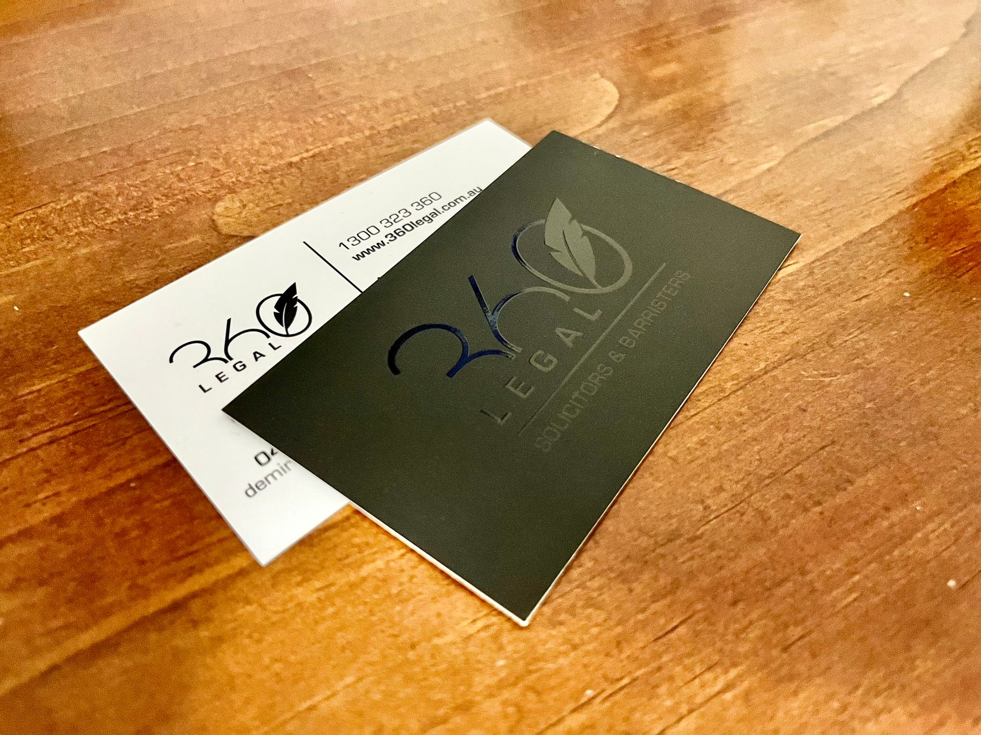 Two business cards on wood surface, one black, one white, featuring 