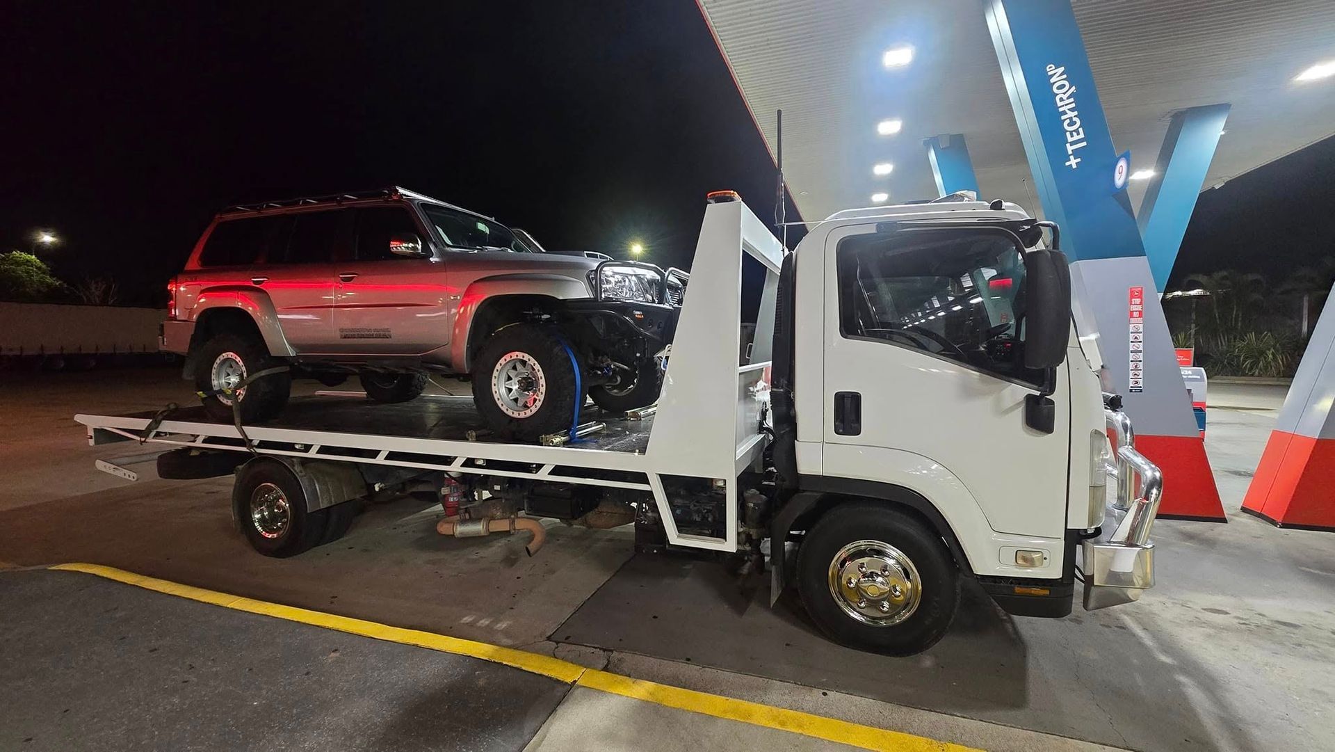 Tow Truck Carrying a Silver Suv at a Gas Station at Night — GTS - Gardiner Transport Solutions in Berserker, QLD