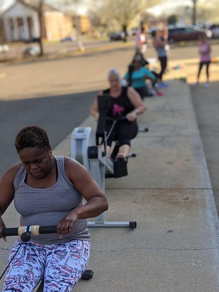 A group of women are rowing rowing machines on a sidewalk.