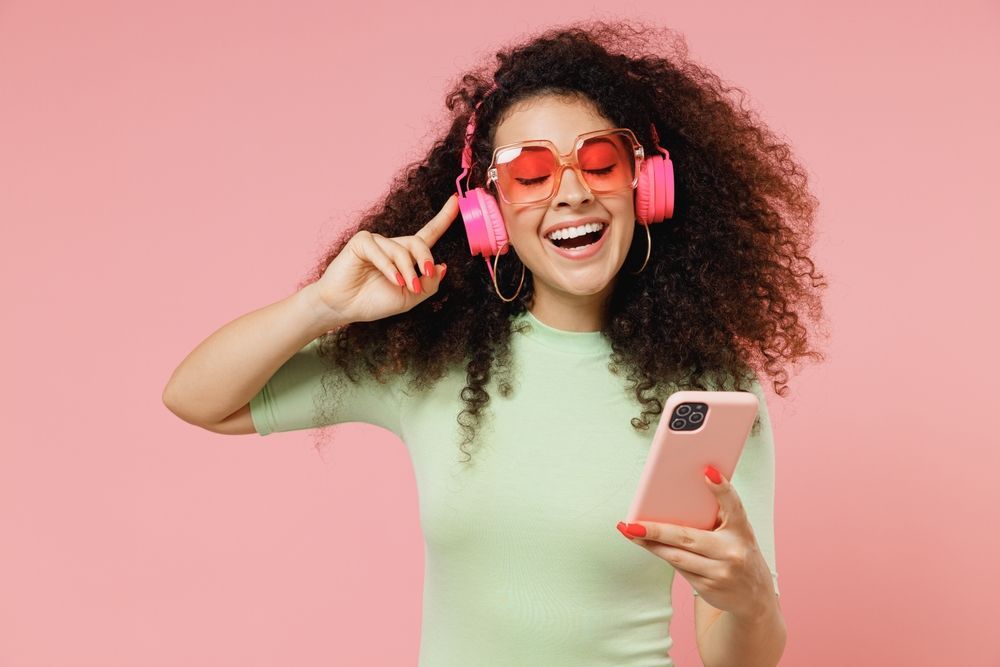 A woman wearing headphones and sunglasses is holding a cell phone.