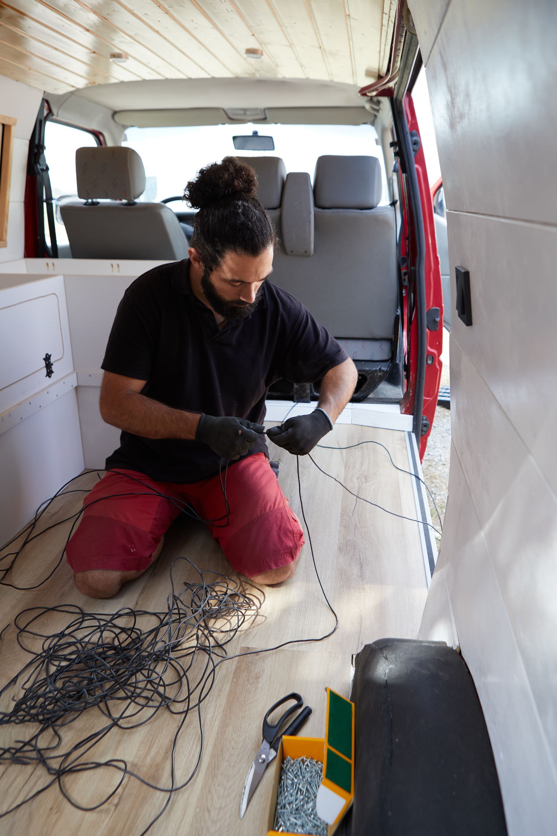 A man works on a van in the middle of an RV repair shop, surrounded by tools and equipment.