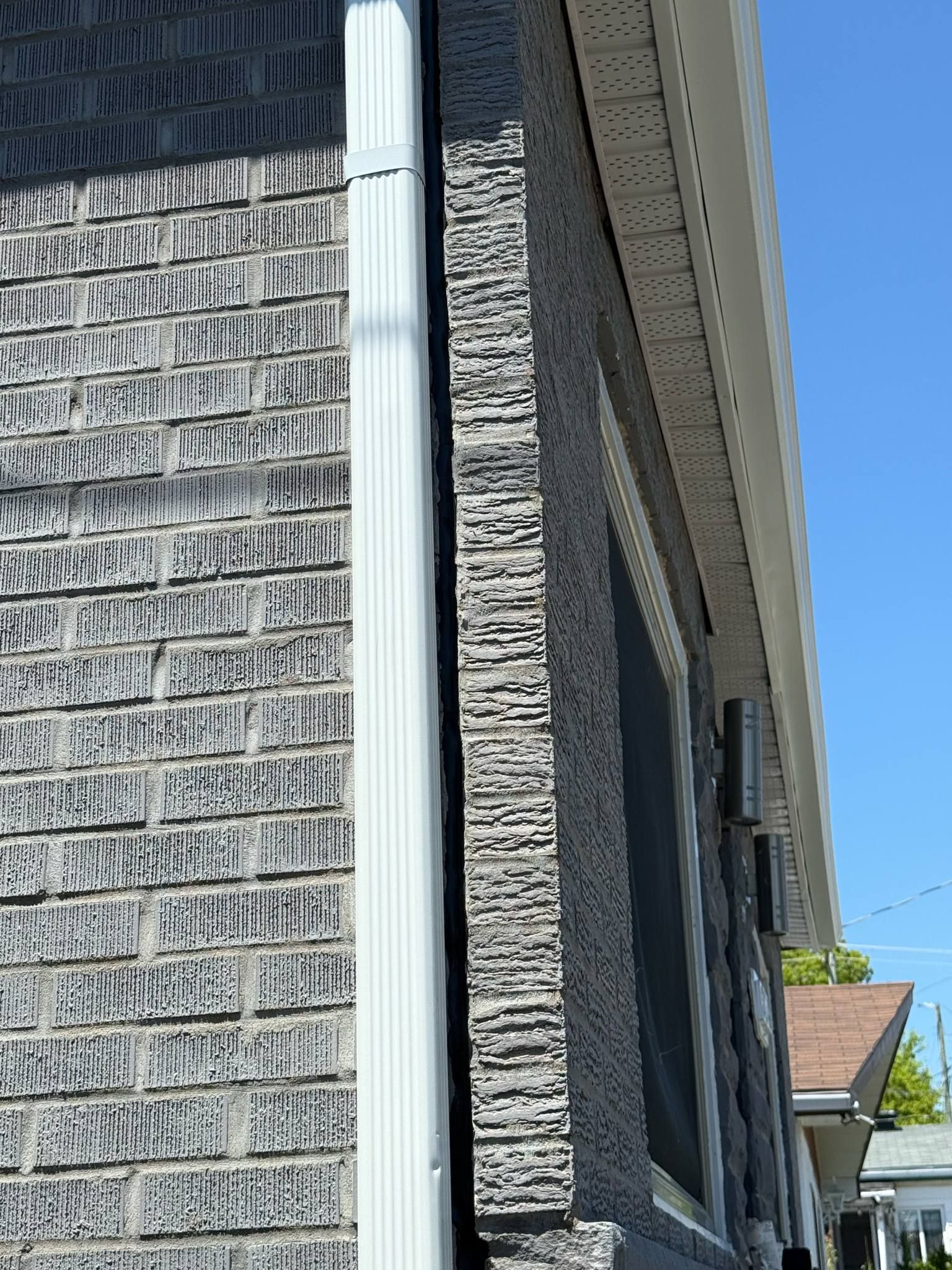 Gros plan sur l'angle d'une maison en briques grises avec des moulures blanches et une fenêtre, vue d'en bas