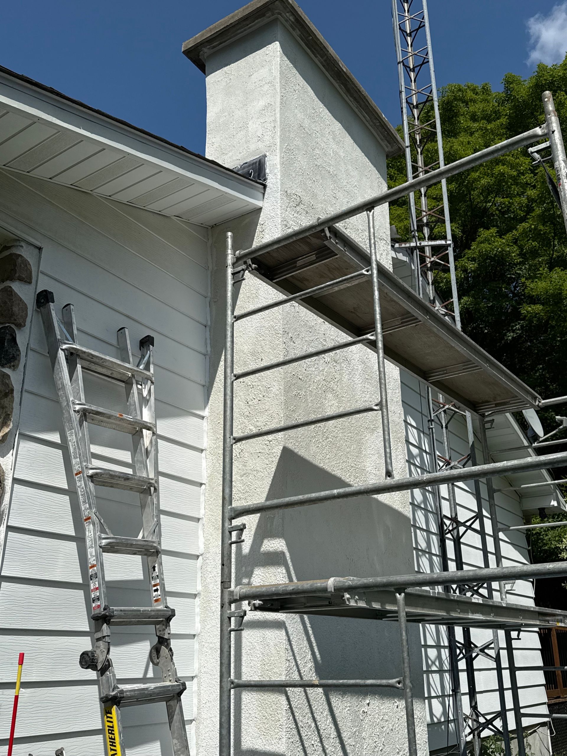Échafaudages près de la cheminée d'une maison blanche sous un ciel bleu clair