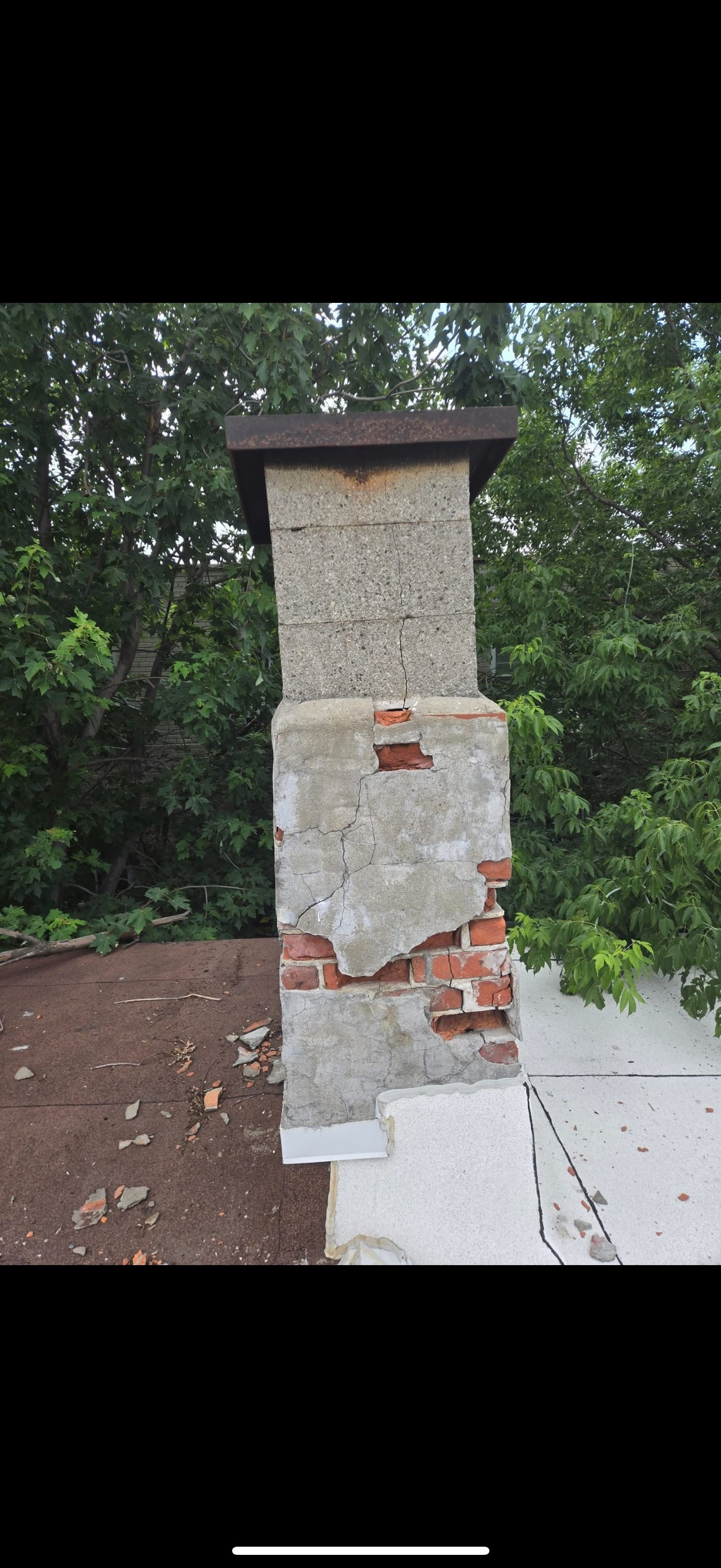 Pilier en briques et en pierres endommagé, situé à côté d'une allée en béton sous des arbres.