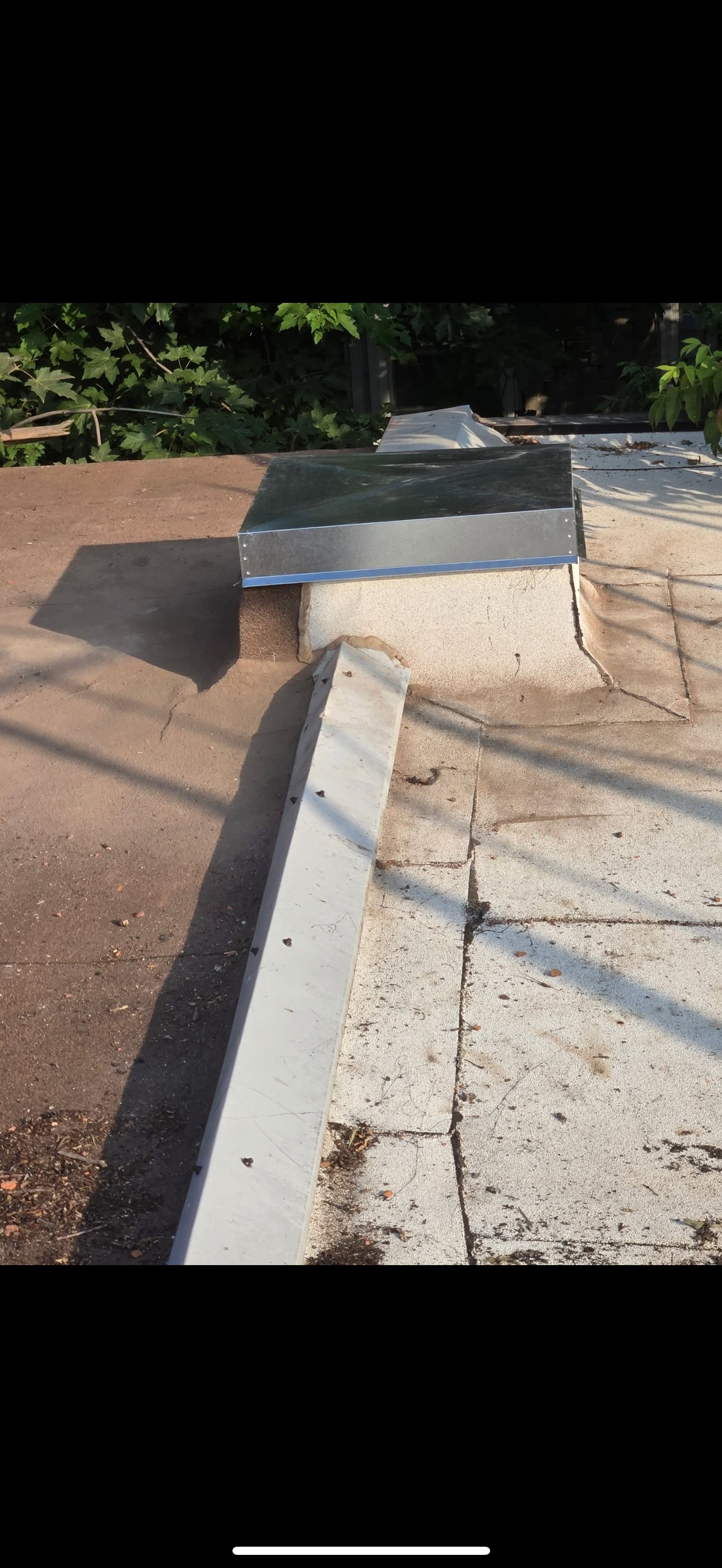 Rampe extérieure en béton longeant une allée, avec un muret et l'ombre des arbres au soleil