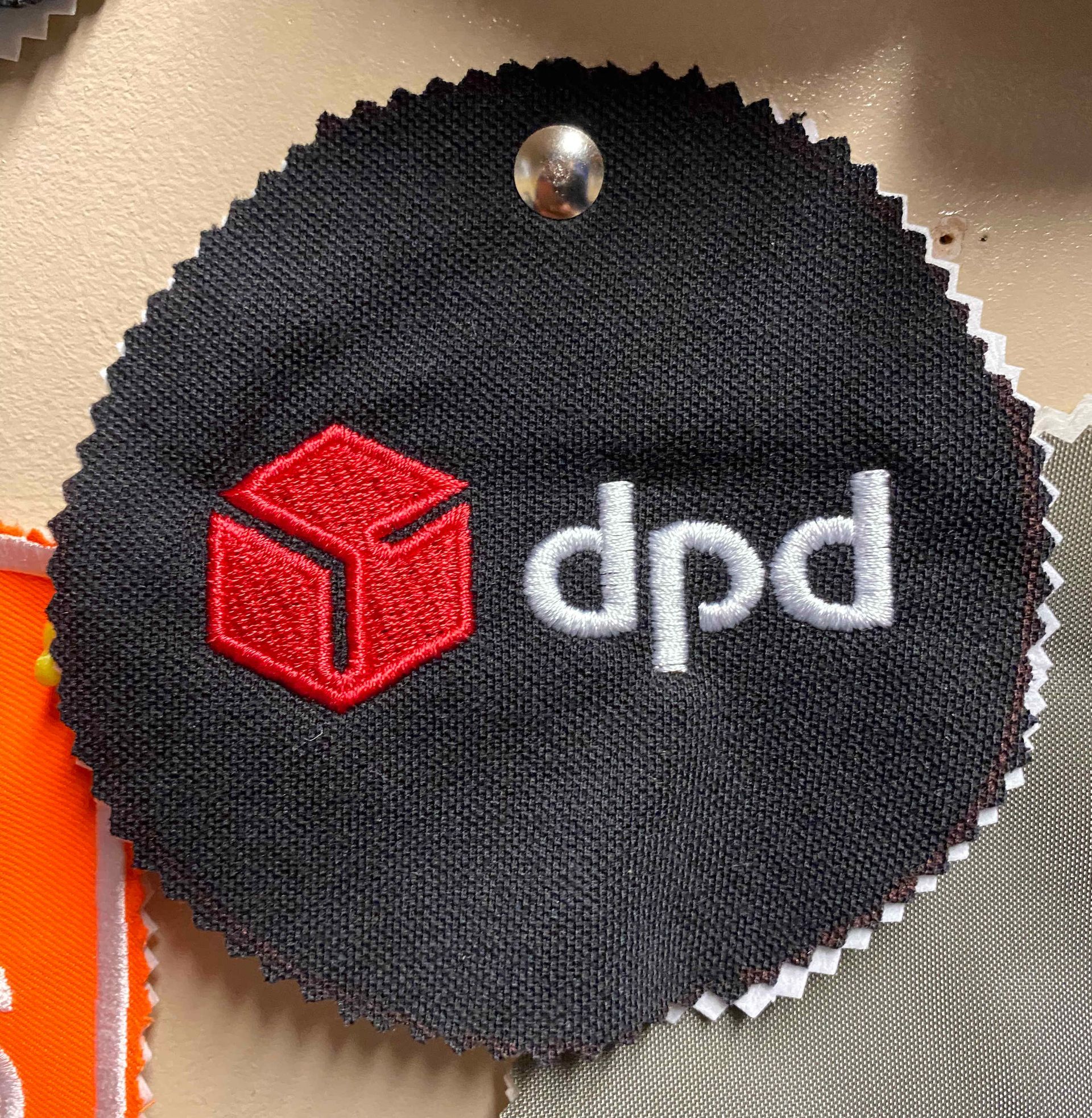 Black fabric swatch with embroidered DPD logo: red cube and white 