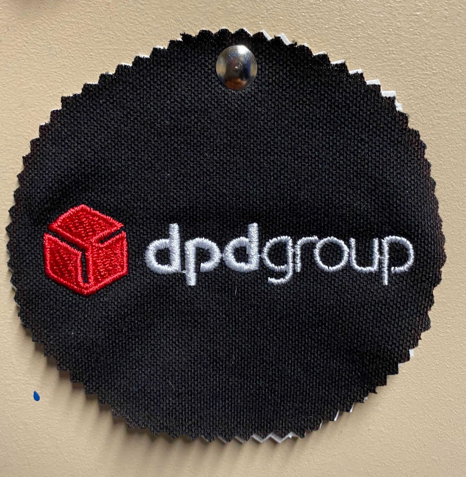 Black circular patch with the embroidered red cube logo and 