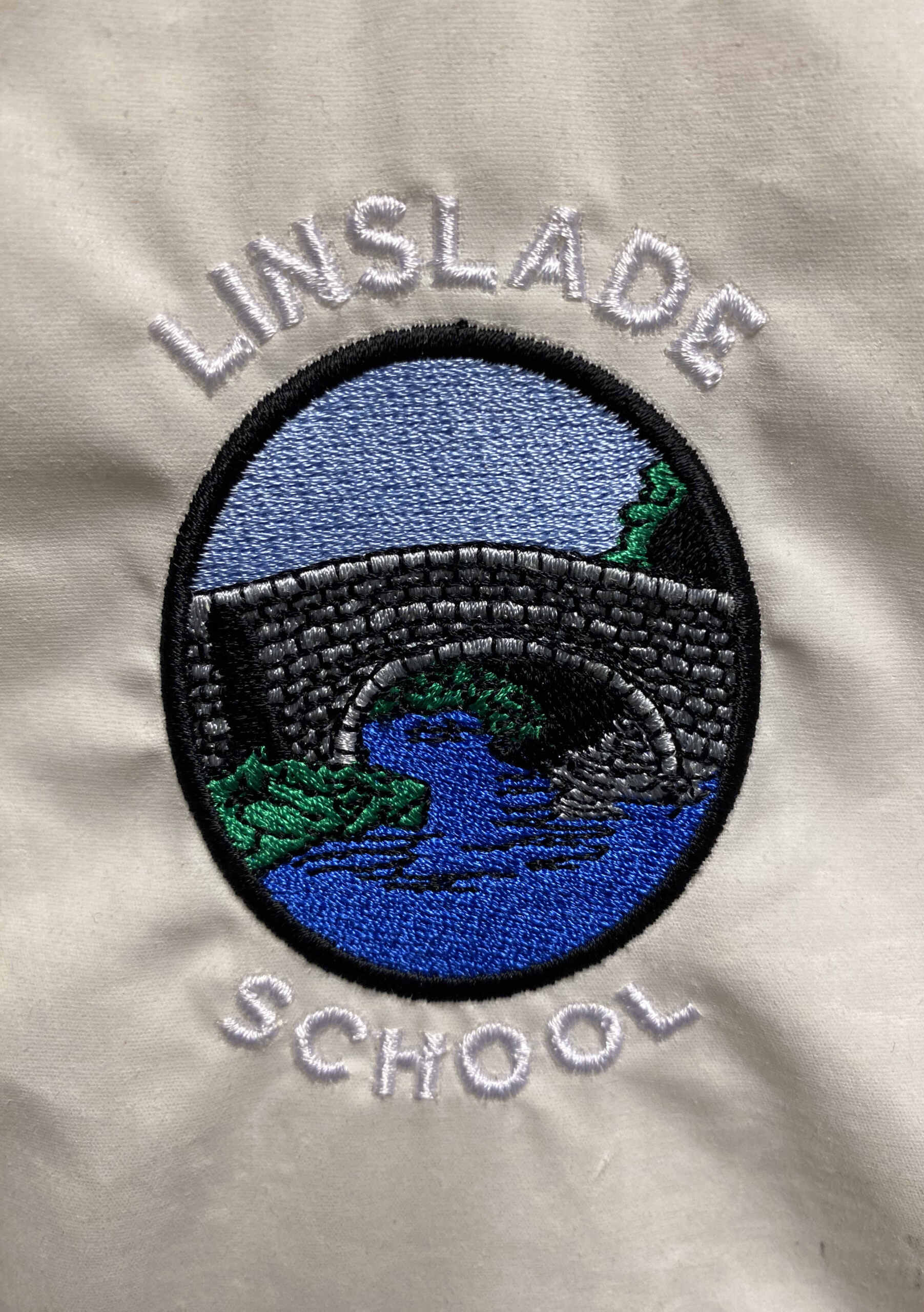 Embroidered school badge with a stone bridge over blue water, with 