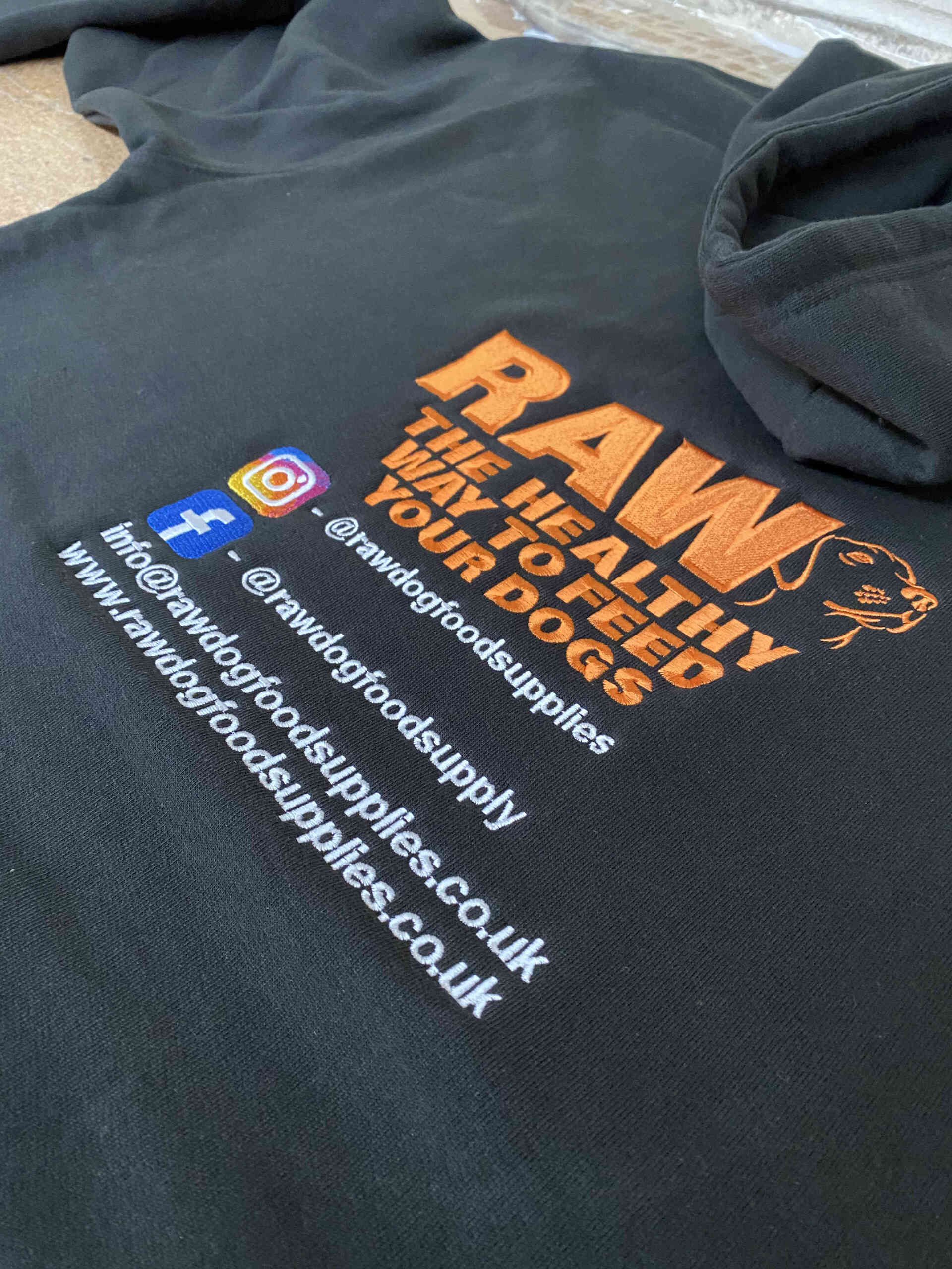 Black hoodie with an embroidered logo  Contact information and social media icons are also present.