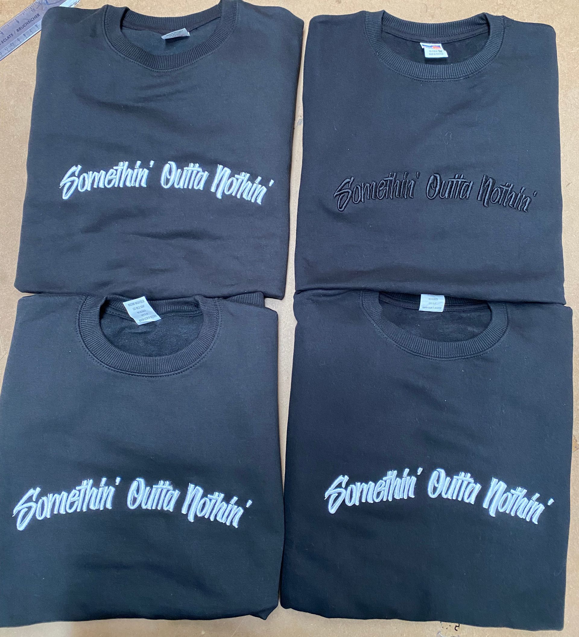 Four black sweatshirts with white  and black 3D embroidered text reading 