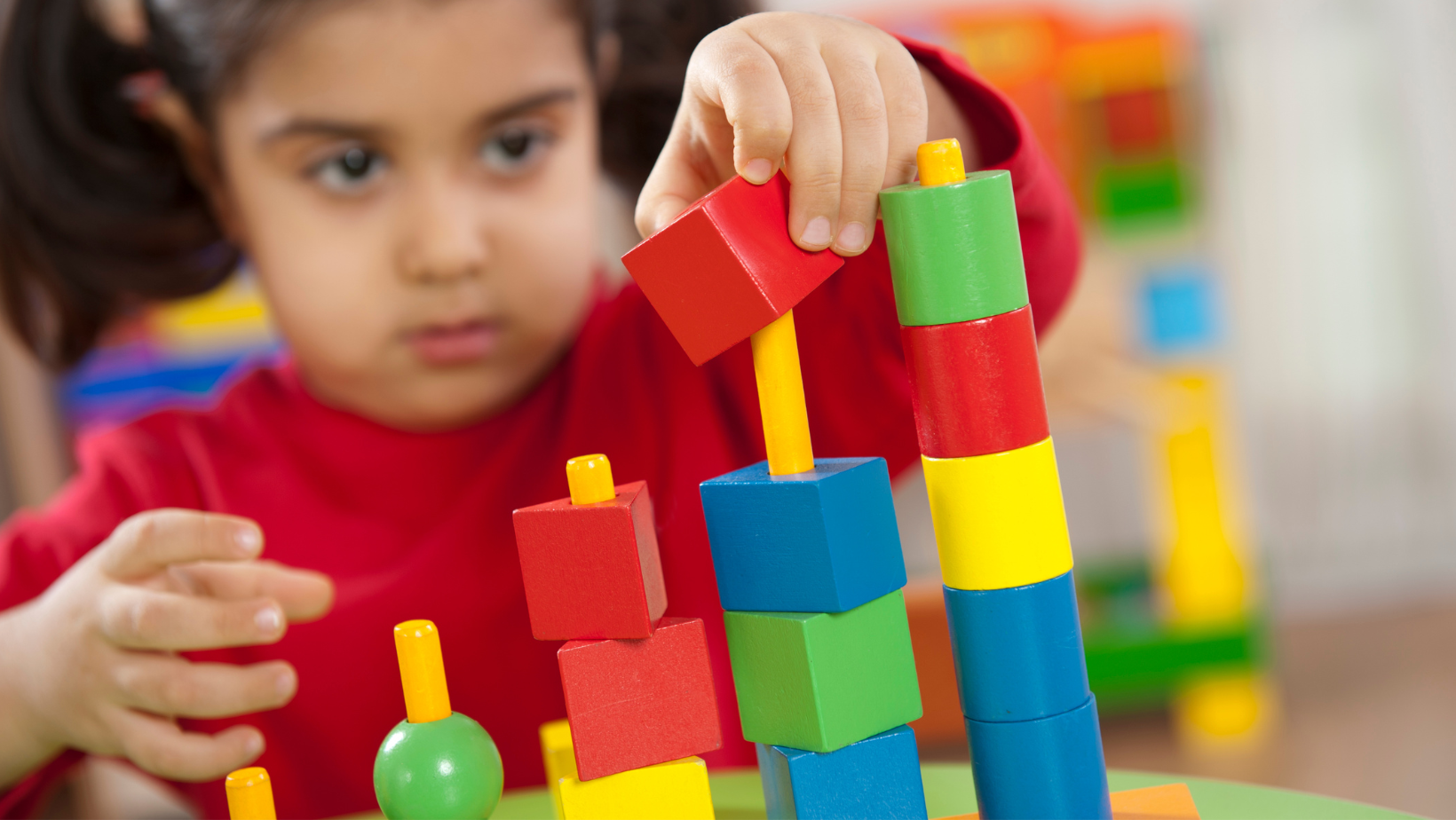 Child stacking colorful wooden blocks on a table, focused expression.