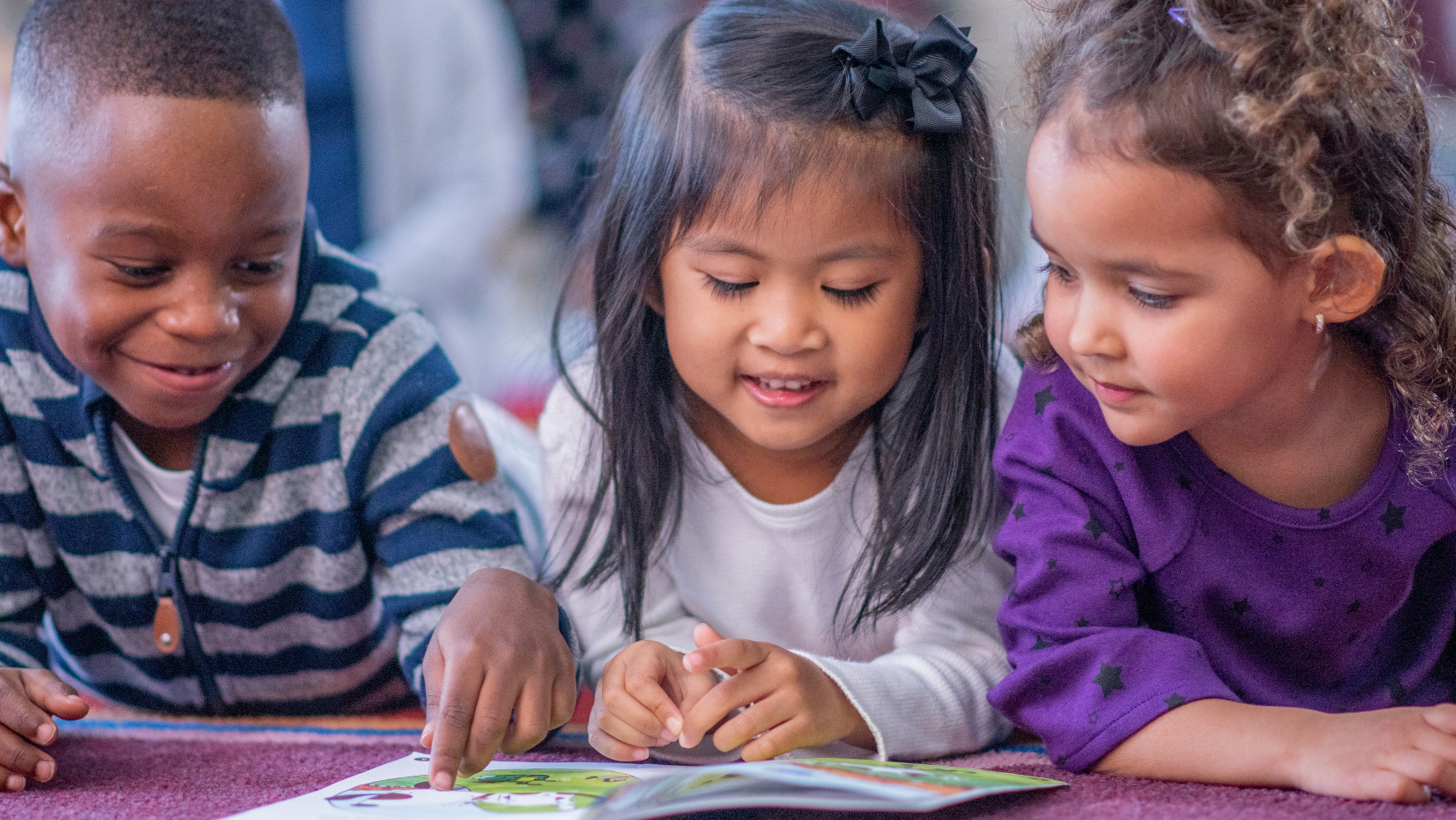 Three children looking at a book together, smiling.