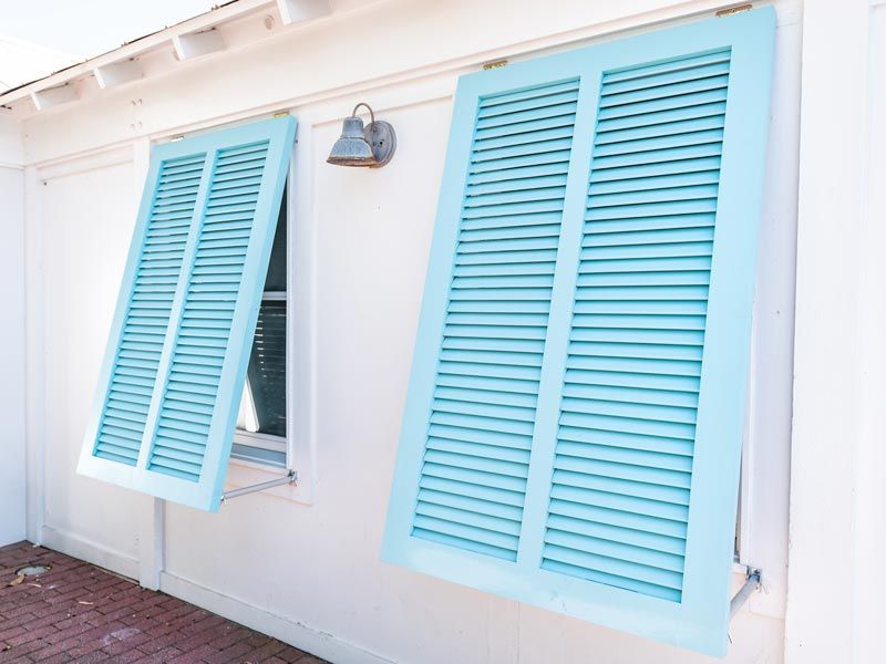 Blue shutters on a white house, one window open outward beside a wall light.