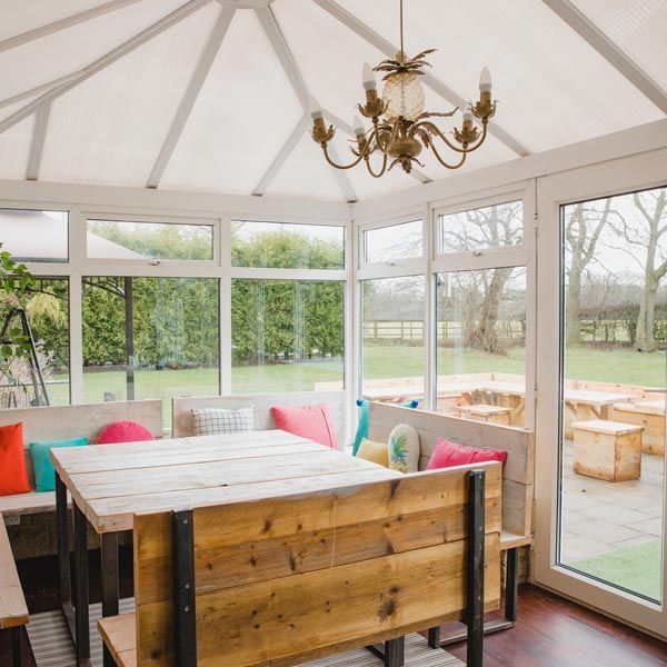 Sunroom dining area with wooden table, colorful bench cushions, and garden views through large windows