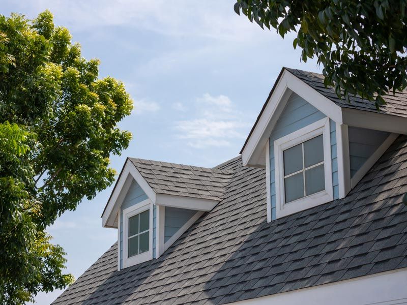 Gray shingled house roof with two dormer windows under a clear blue sky