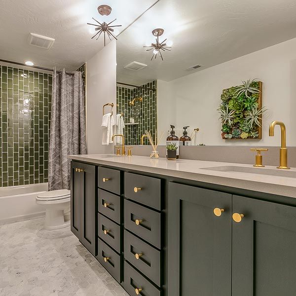 Modern bathroom with green cabinets, gold fixtures, and green tile shower walls