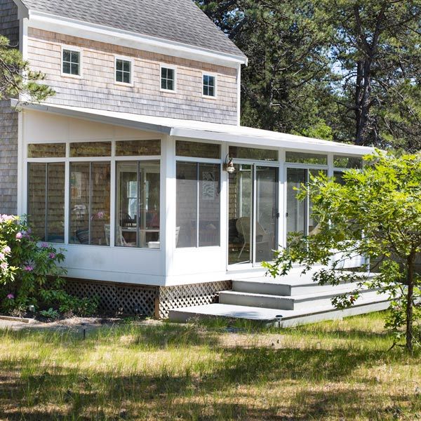 White house with screened porch and steps surrounded by trees and grass