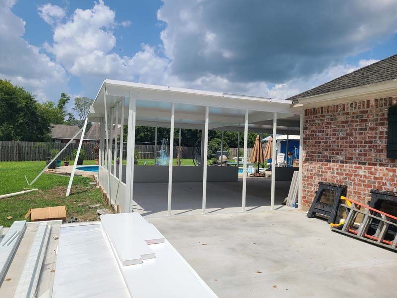 Backyard patio under construction with white roof frame beside a brick house and concrete slab