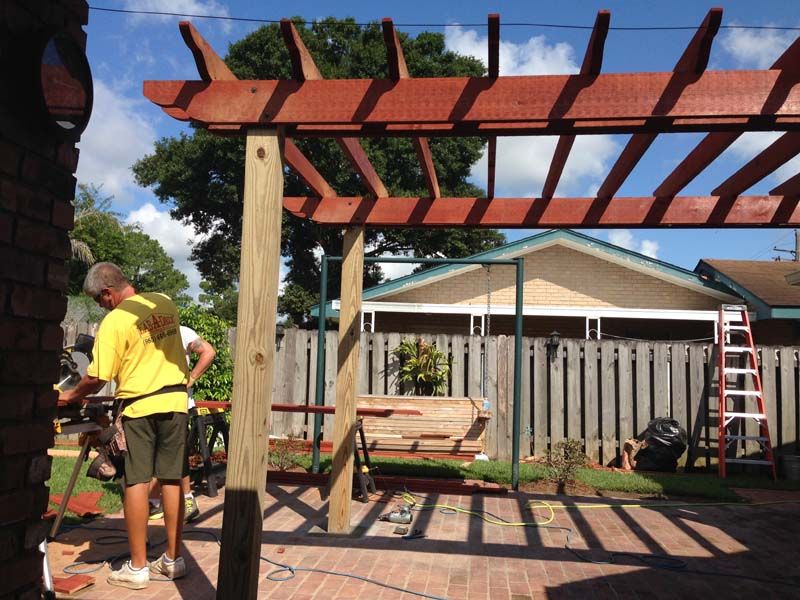 Two workers assembling a wooden pergola in a backyard under a blue sky