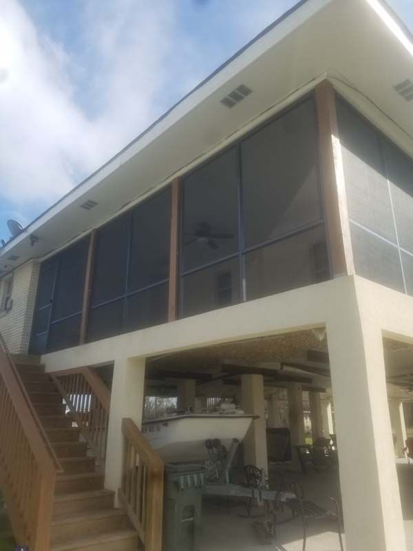 Modern elevated house with stairs, screened windows, and a shaded open area underneath