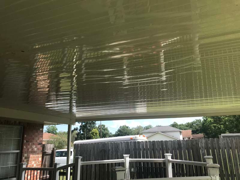 Covered patio with reflective ceiling, wooden fence, and a glimpse of backyard beyond the railing