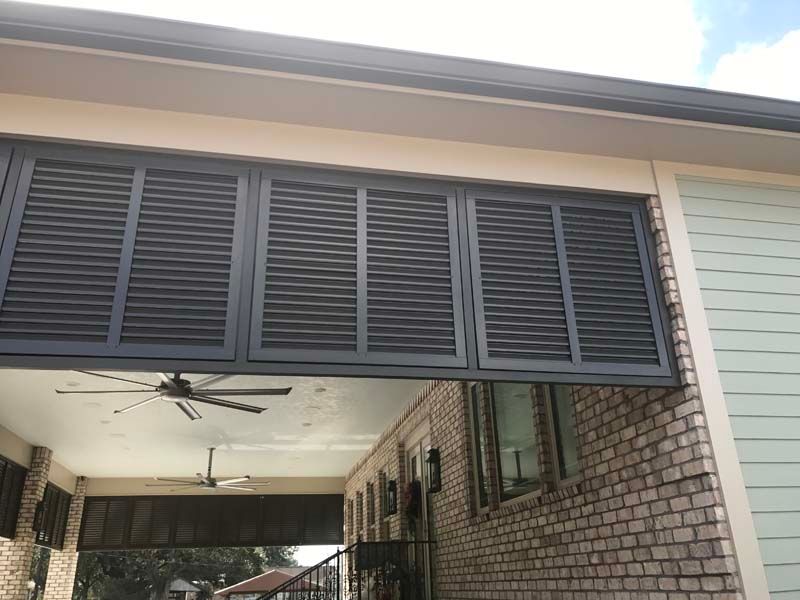 Garage-style breezeway with open louvered shutters, ceiling fan, and brick wall under a roof overhang