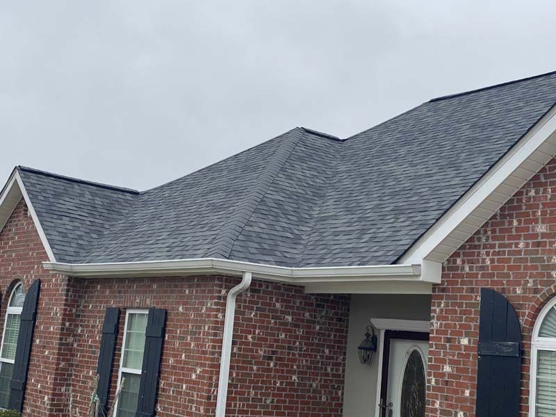 Brick house with gray shingle roof and white trim under an overcast sky