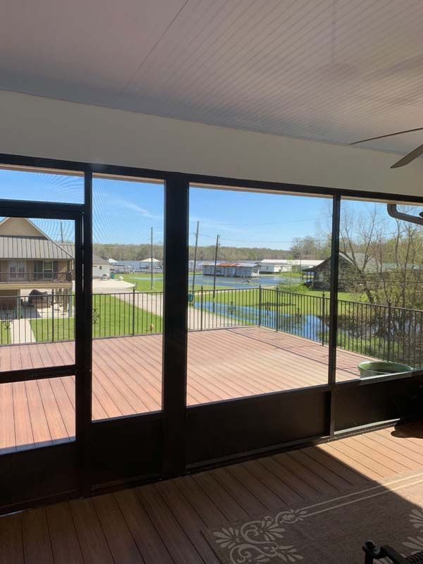 Screened porch overlooking a backyard with a wooden deck, lawn, and blue sky beyond.