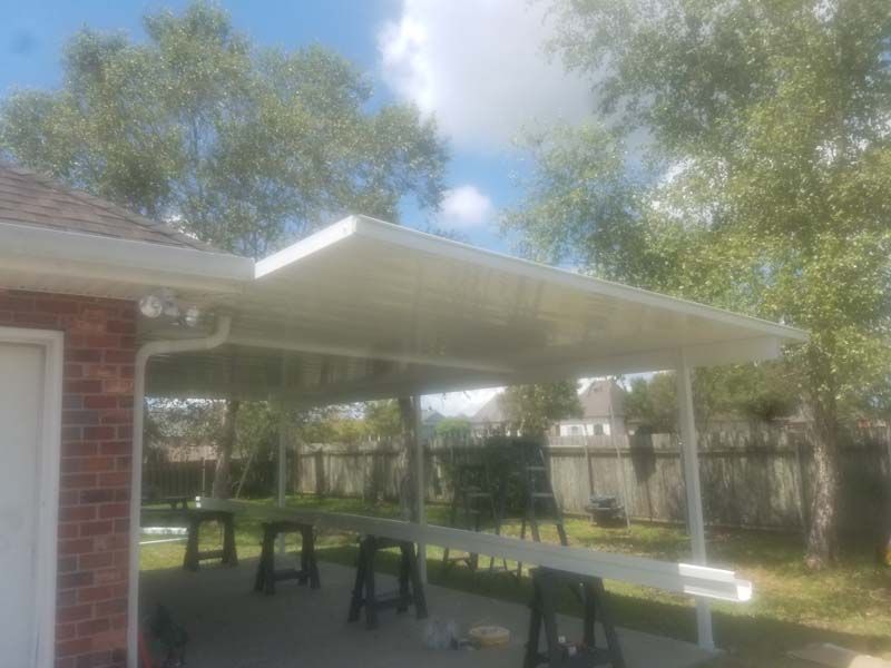 Covered outdoor picnic area with tables beside a brick house and trees