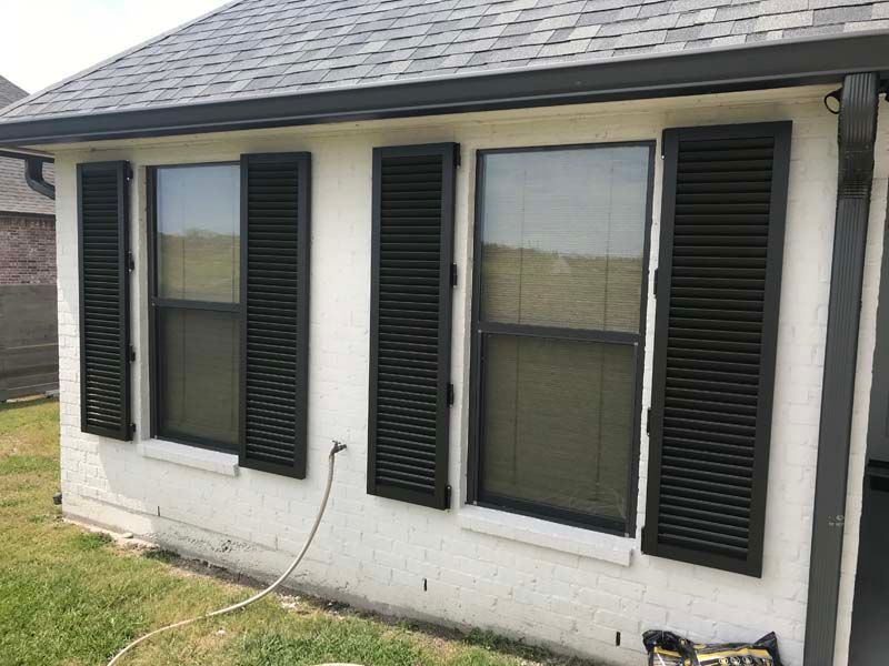 House exterior with three black-shuttered windows and a white cable on the grass.