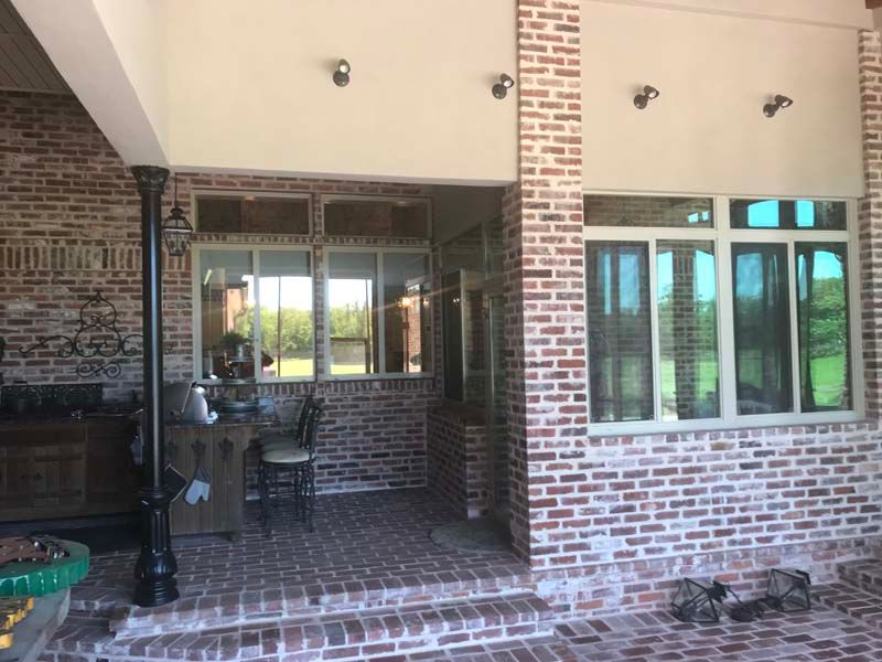Brick patio with covered outdoor seating area, windows, and brick columns beside a house
