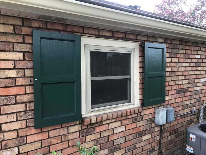 Brick house exterior with a white-framed window and dark green shutters