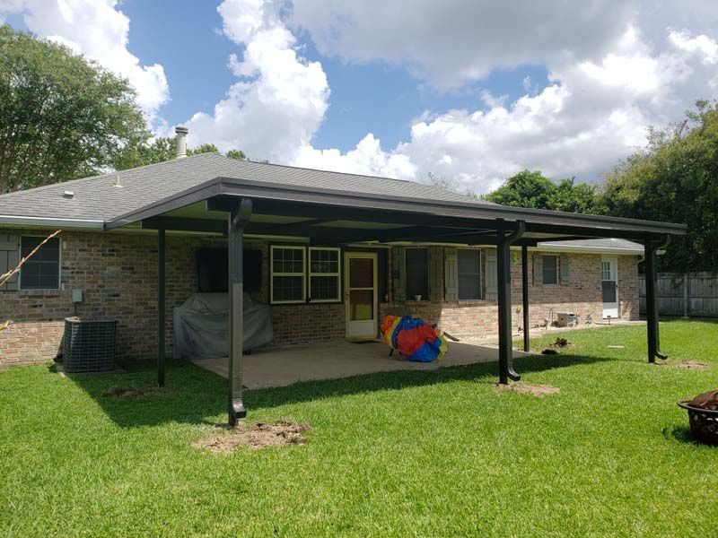 Brick house with covered back patio, green lawn, and cloudy sky