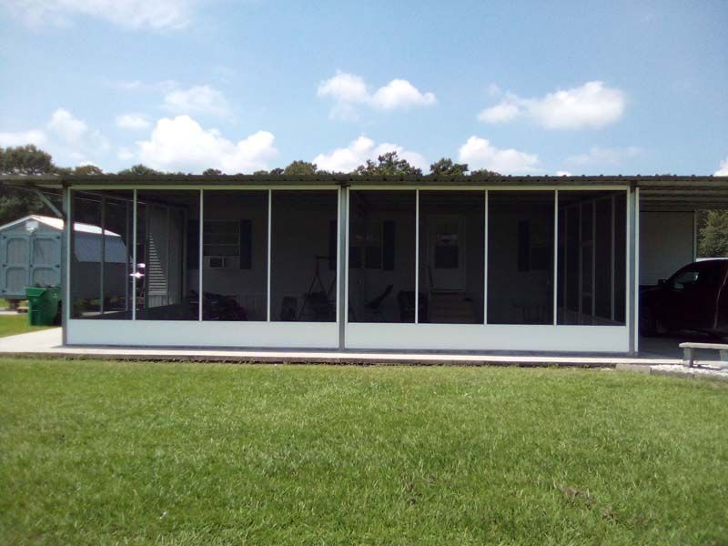 Single-story screened porch with white posts and large windows behind a green lawn.