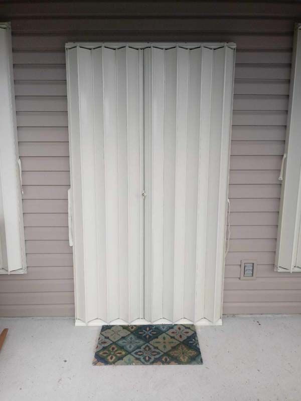White sliding glass door with closed vertical blinds and a small patterned doormat on a porch.