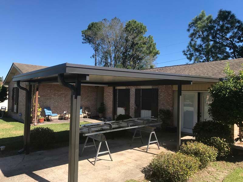 Backyard patio with a covered pergola, folding table, and chairs beside a brick house.