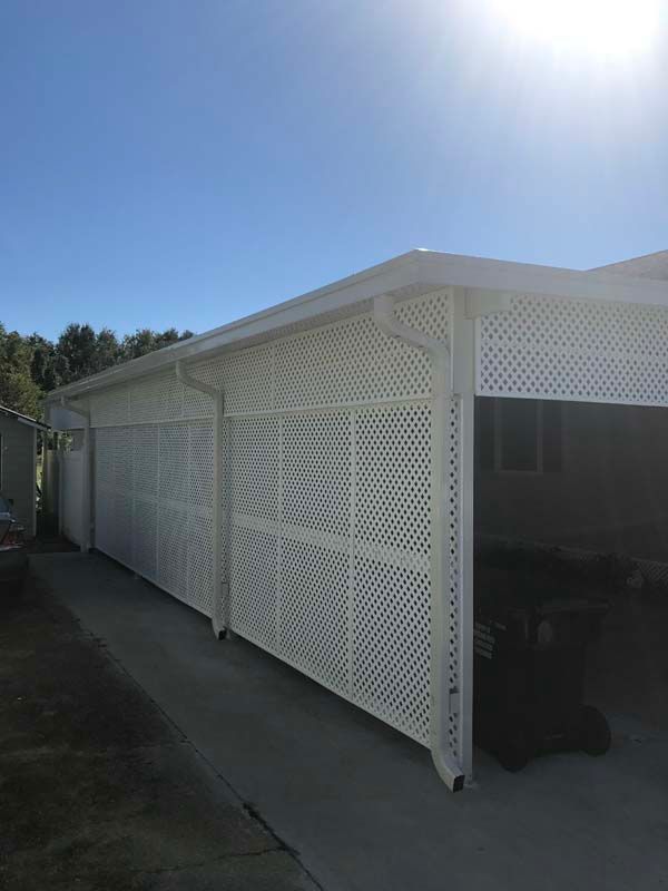 White lattice exterior walls and carport attached to a small building under a bright blue sky.