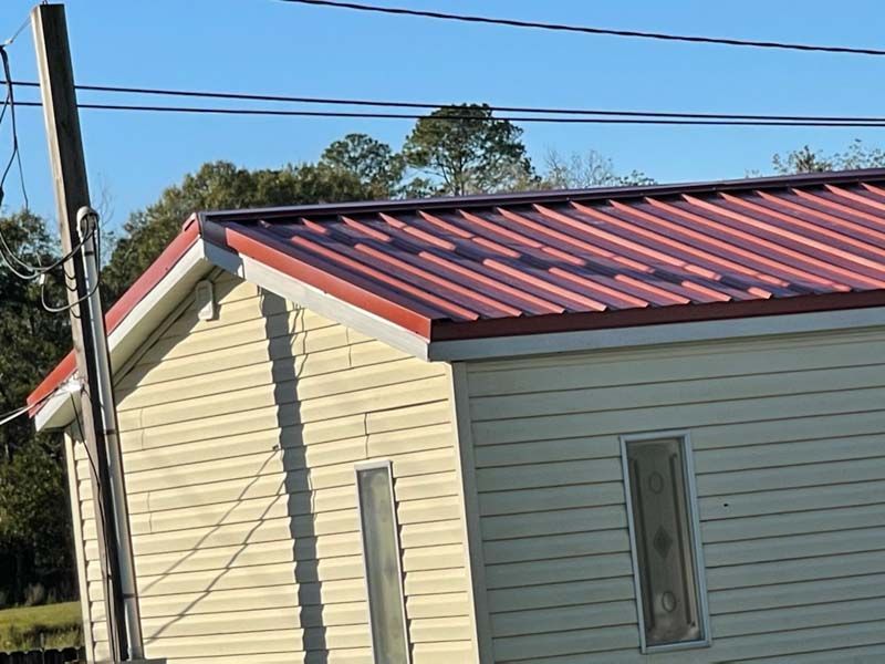 Cream-sided house with a red metal roof under a blue sky and power lines above