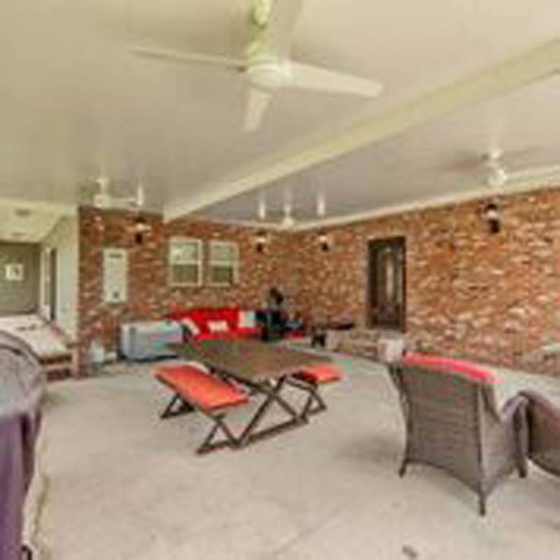 Covered patio with brick walls, ceiling fans, wicker seating, and red cushions